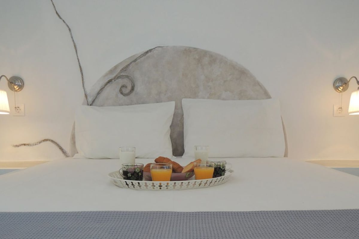 A bed with a white headboard, two wall-mounted lamps, and a tray with breakfast items.