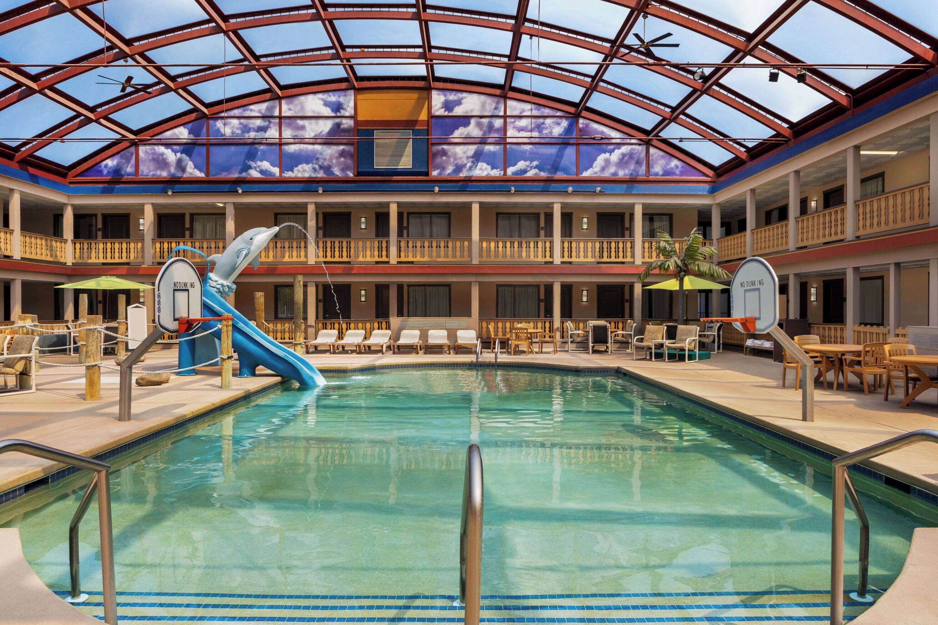 An indoor swimming pool with a dolphin slide, lounge chairs, and a glass ceiling.