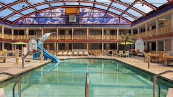An indoor swimming pool with a dolphin slide, lounge chairs, and a glass ceiling.