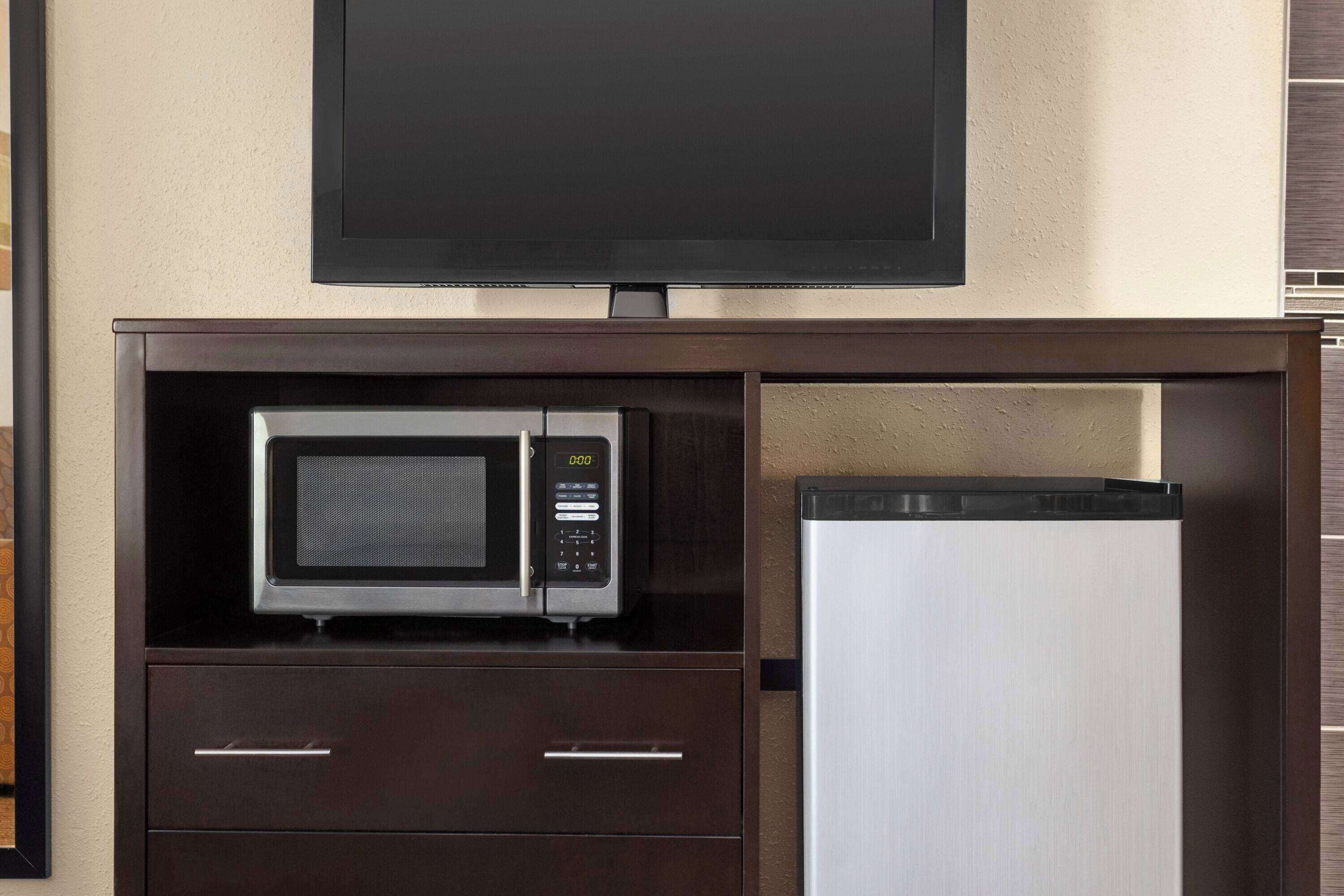 A kitchenette with a microwave, a refrigerator, and a flat-screen TV mounted on the wall.