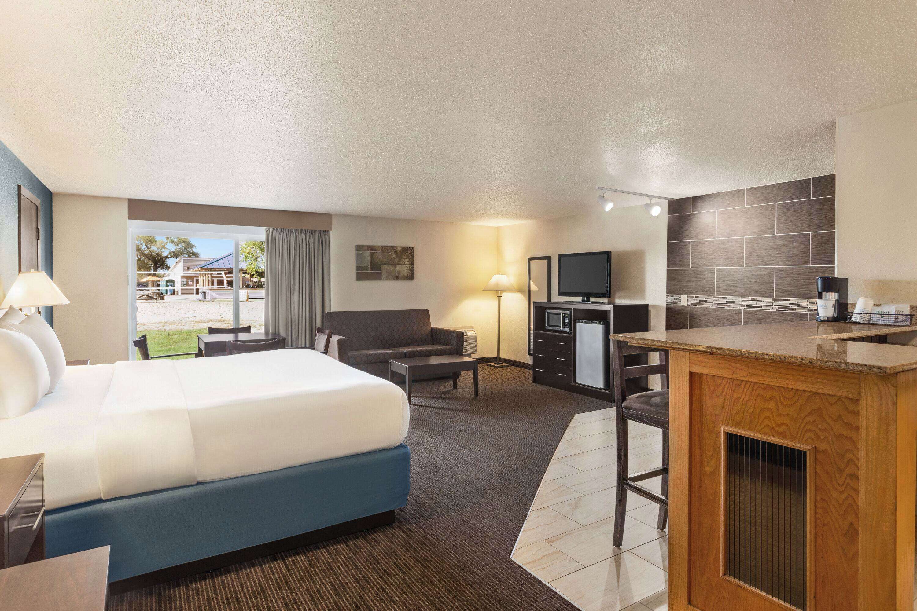 A hotel room with a large bed, a sofa, a desk, a TV, and a kitchenette.