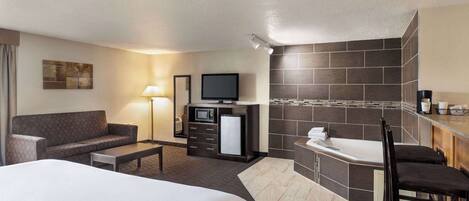 Habitación de hotel con una cama grande, un sofá, un escritorio, microondas, televisión, baño pequeño con bañera y una cafetera.