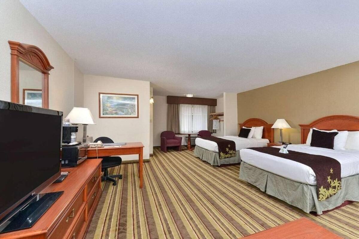 Una habitación de hotel con televisión, escritorio, dos camas, una silla y ventana.