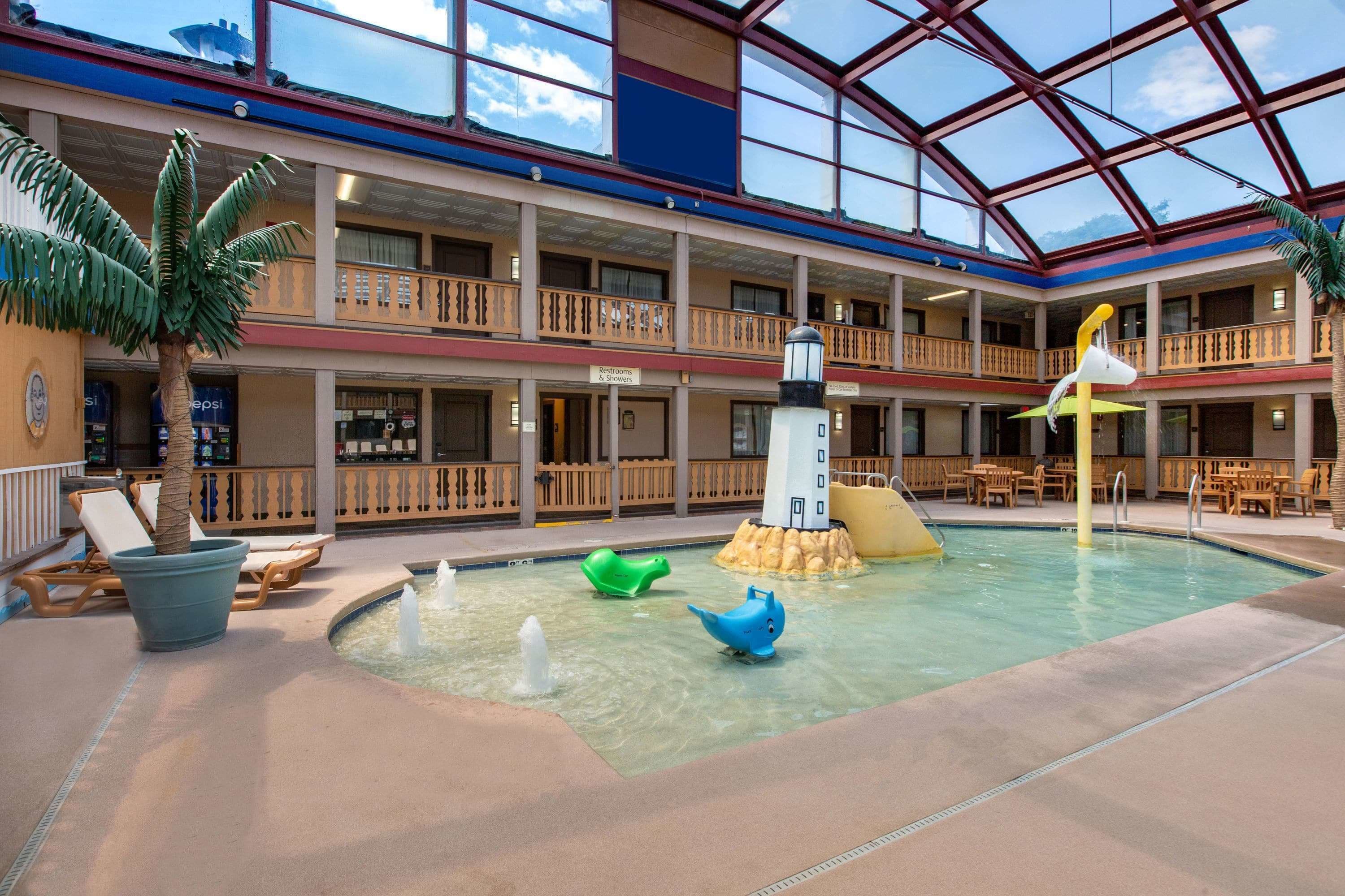A multi-level indoor pool area with a water fountain, lounge chairs, and a lifeguard tower.