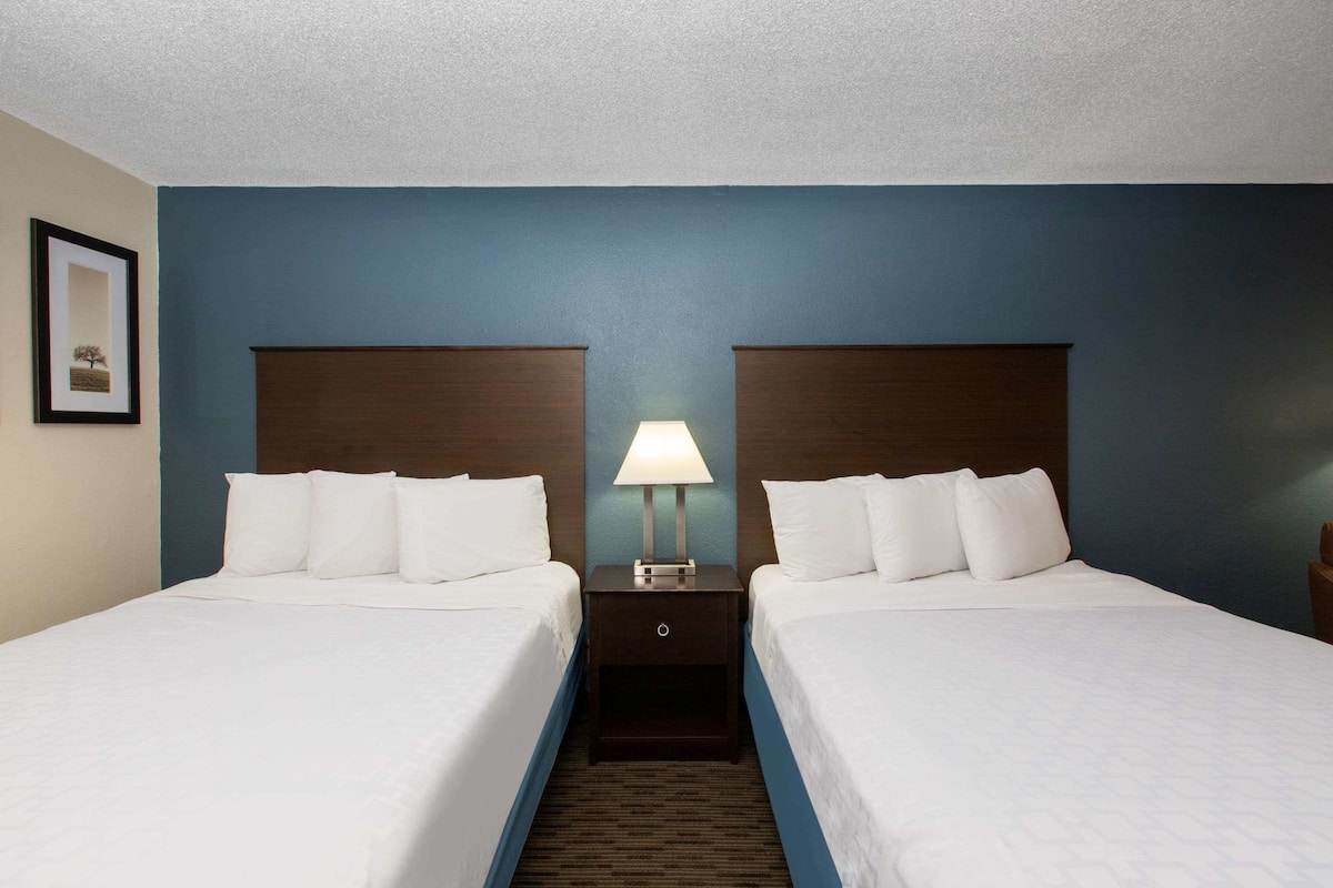 Habitación de hotel con dos camas, una mesita de noche con lámpara y un cuadro en la pared.
