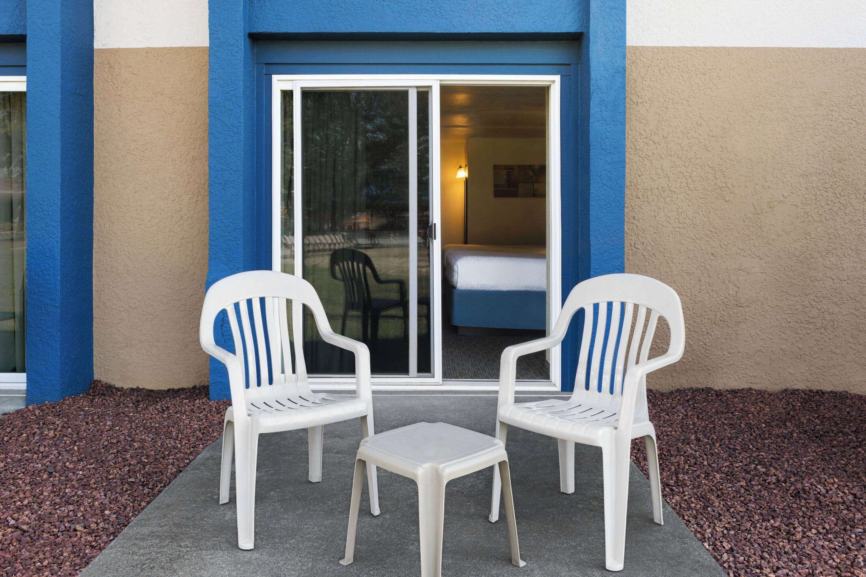 A hotel room with a sliding glass door, two white plastic chairs, and a small table.