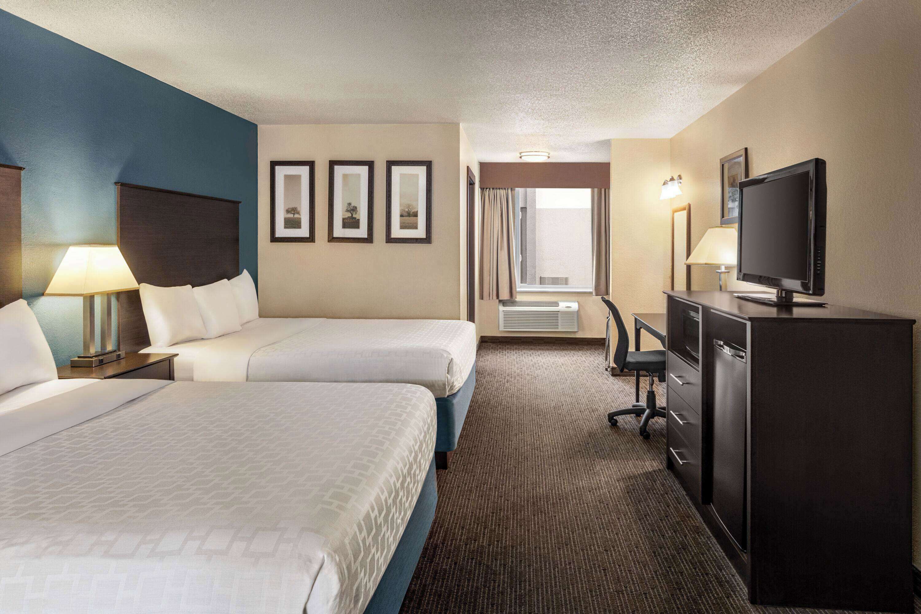 A hotel room with two beds, a desk, a television, and a window with curtains.