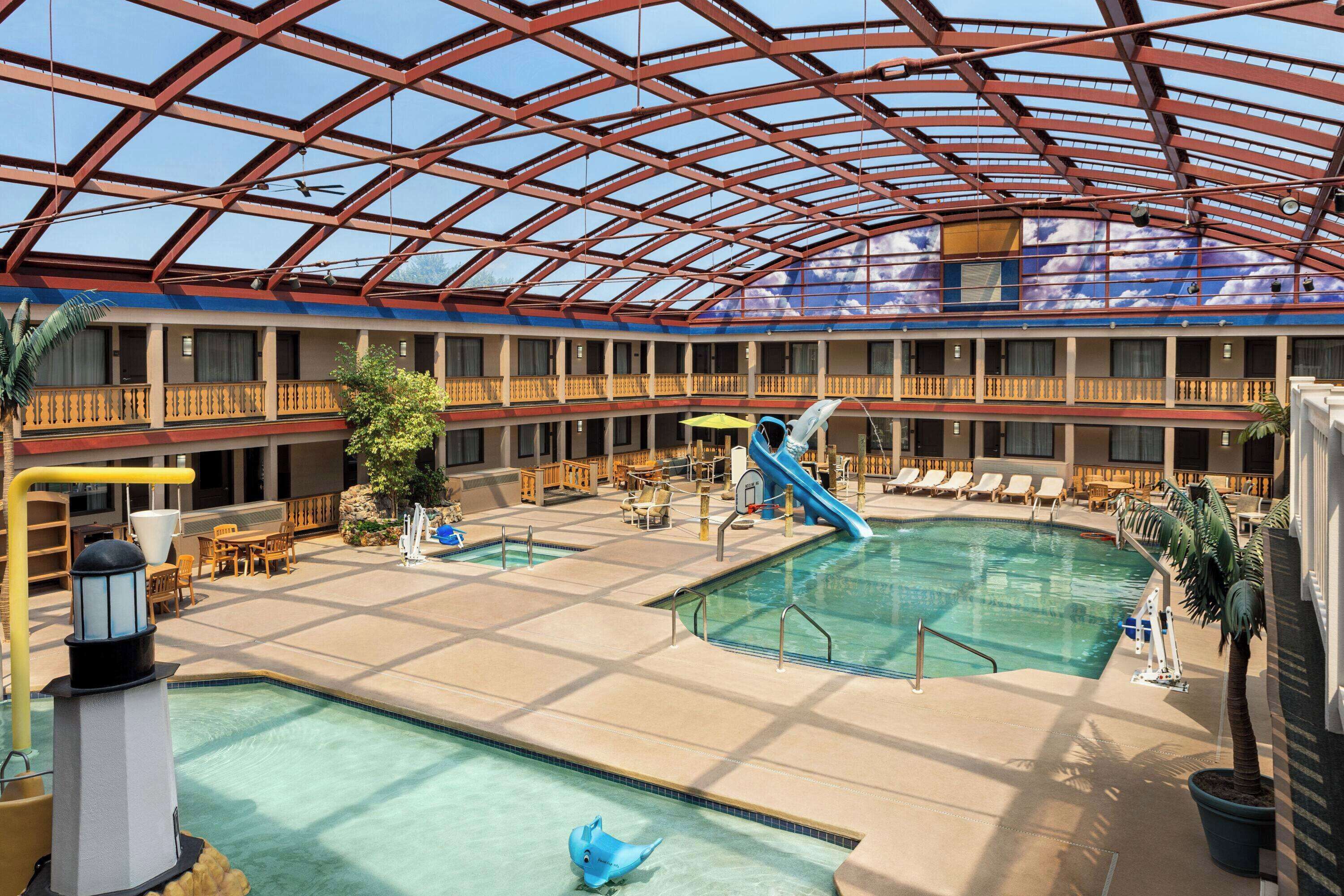 An indoor swimming pool with a slide, lounge chairs, and a glass ceiling.
