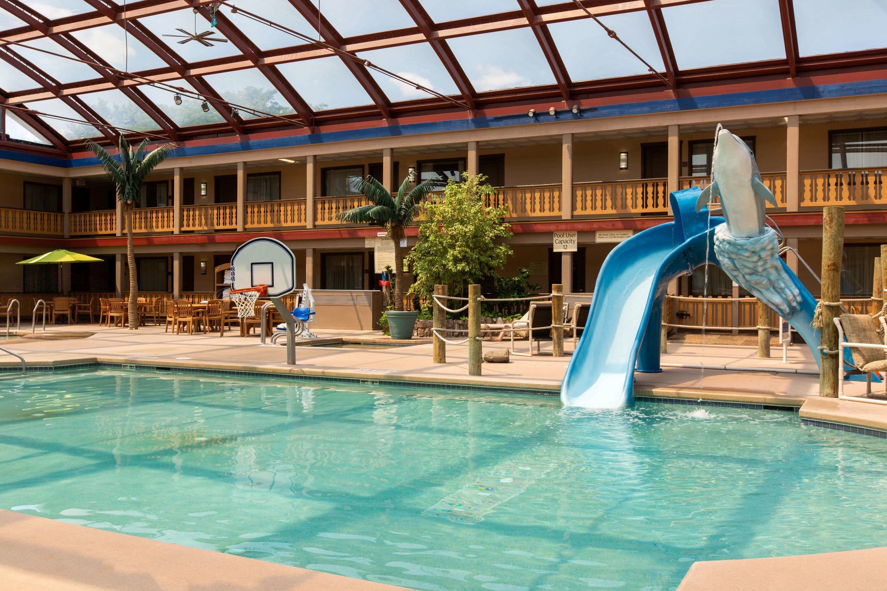 An indoor pool with a blue slide, lounge chairs, and a basketball court.