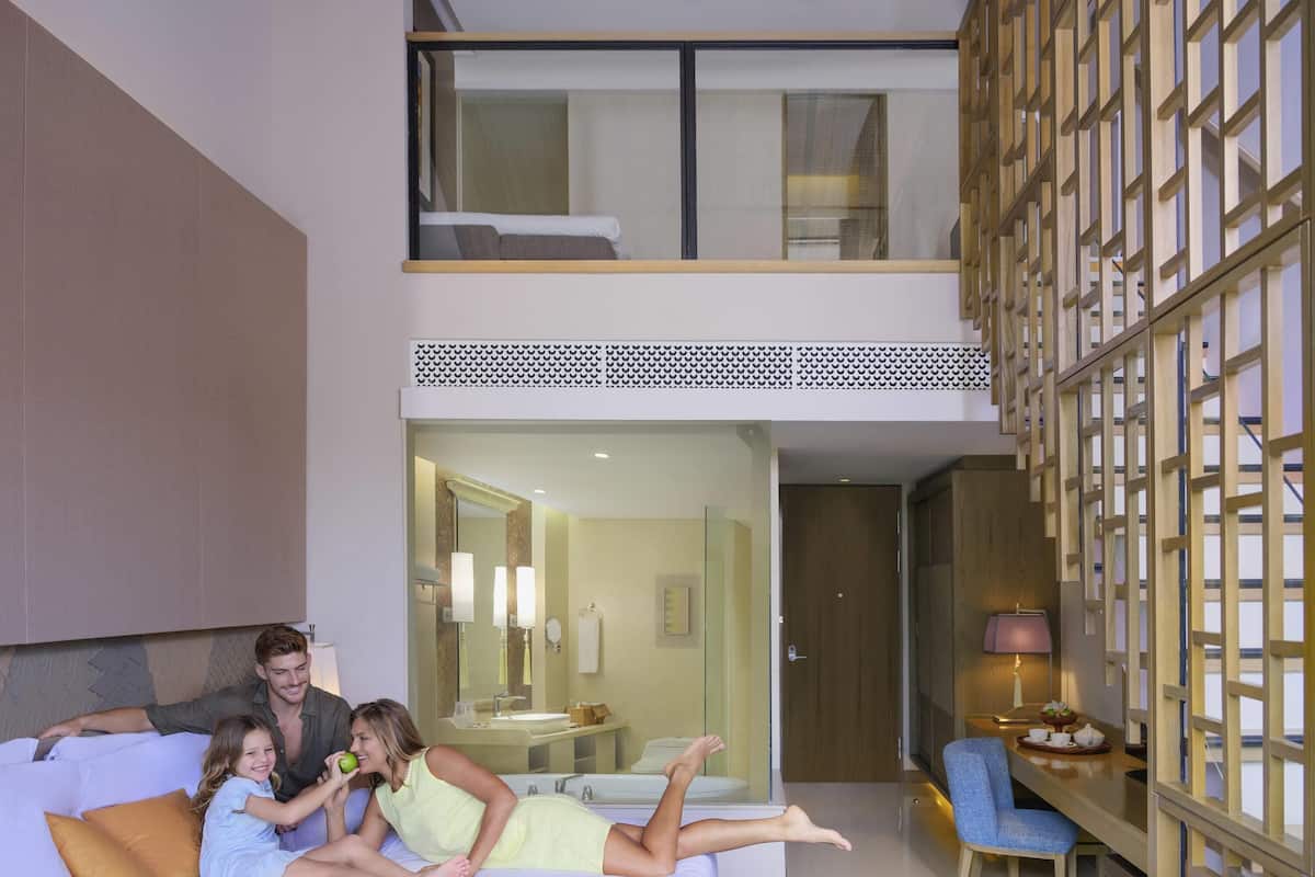 A modern hotel room with a bed, a seating area with a chair, a small table, and a view of the bathroom.