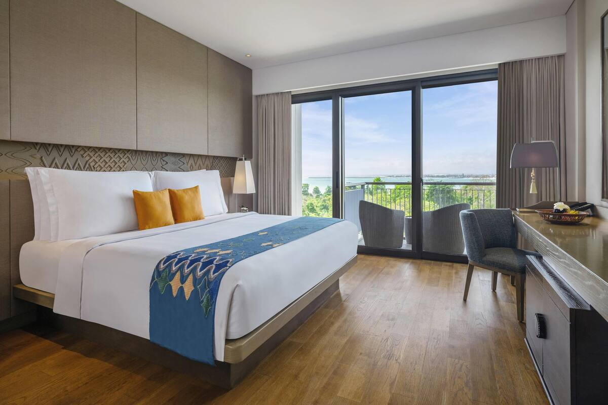 A hotel room with a large bed, a desk with a chair, and a view of the outdoors.