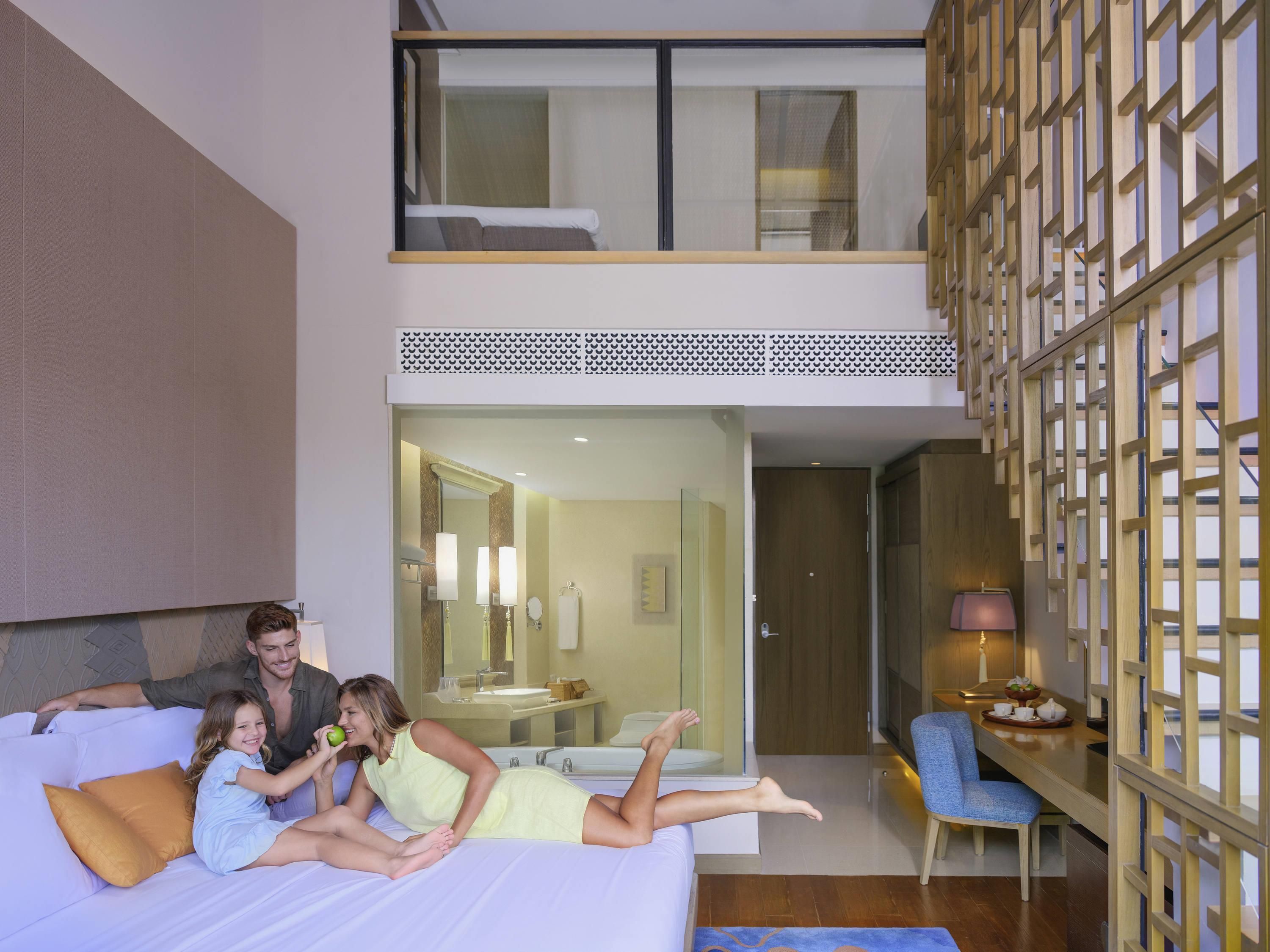 Une chambre d’hôtel moderne comprenant un lit, un coin salon avec un fauteuil, une petite table et une vue sur la salle de bain.