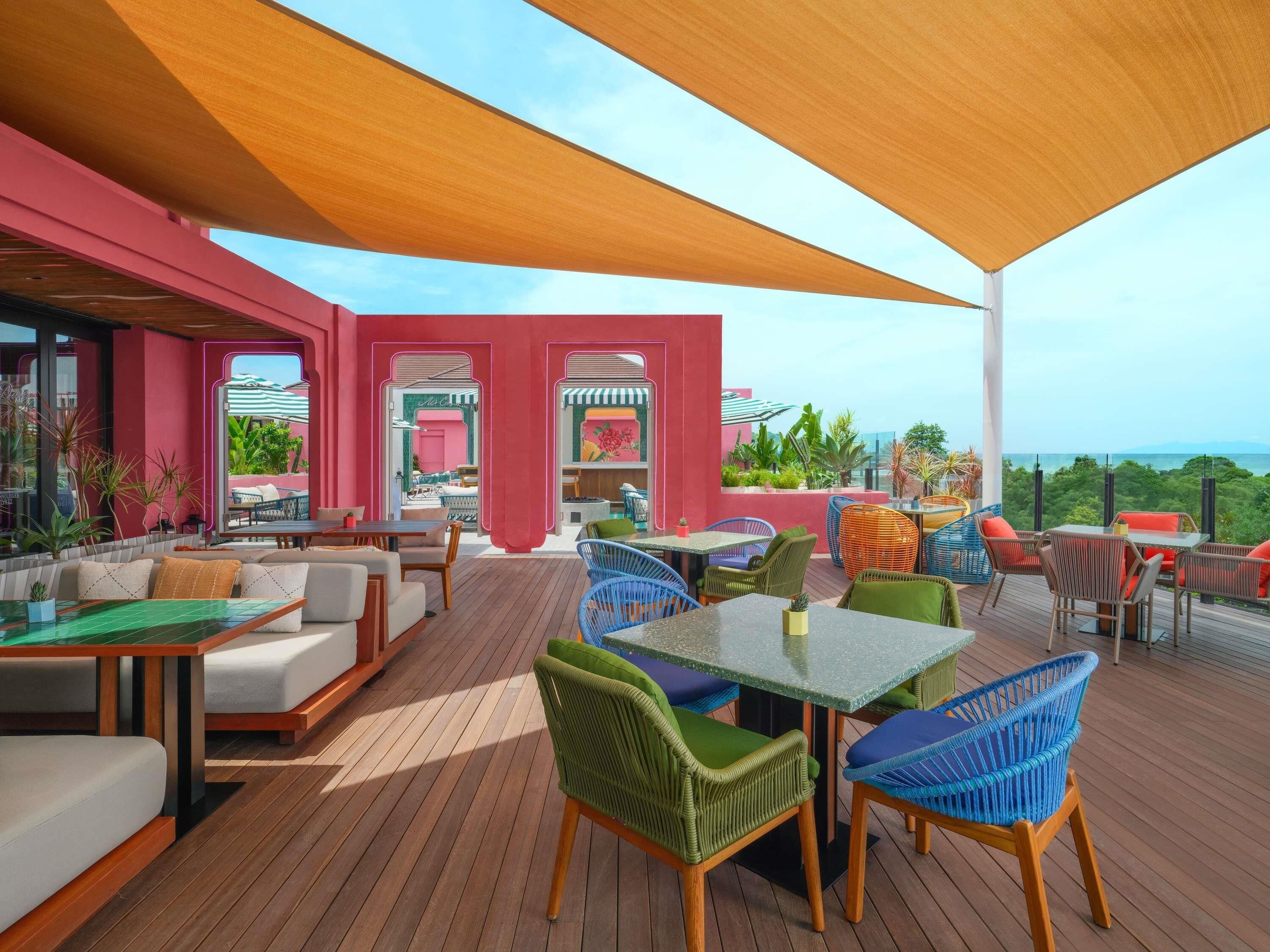 An outdoor patio area with wooden flooring, colorful seating, and a view of the ocean.