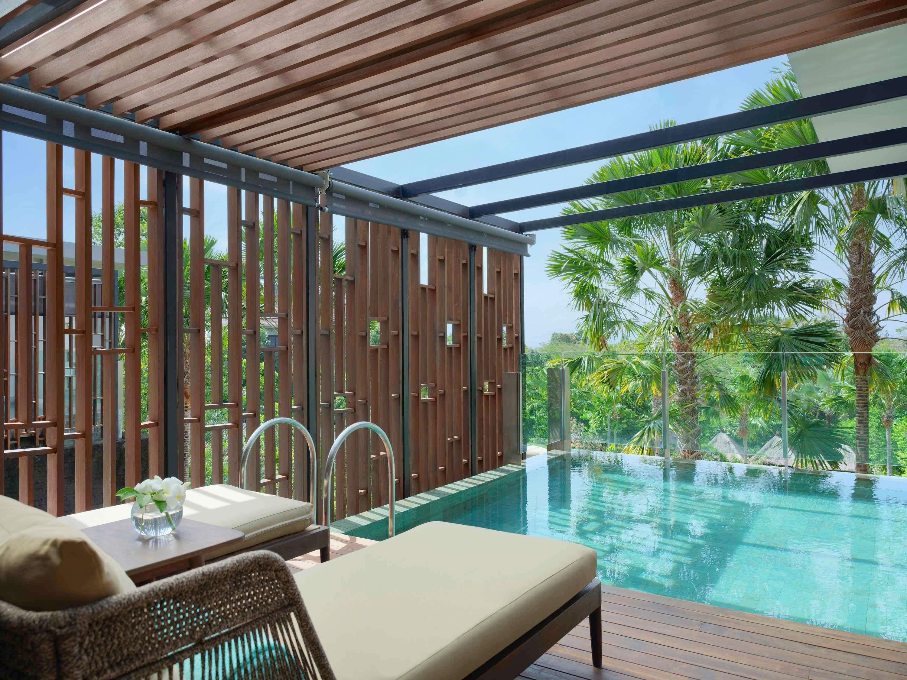 A poolside area with a wooden deck, lounge chairs, and a view of a tropical garden.