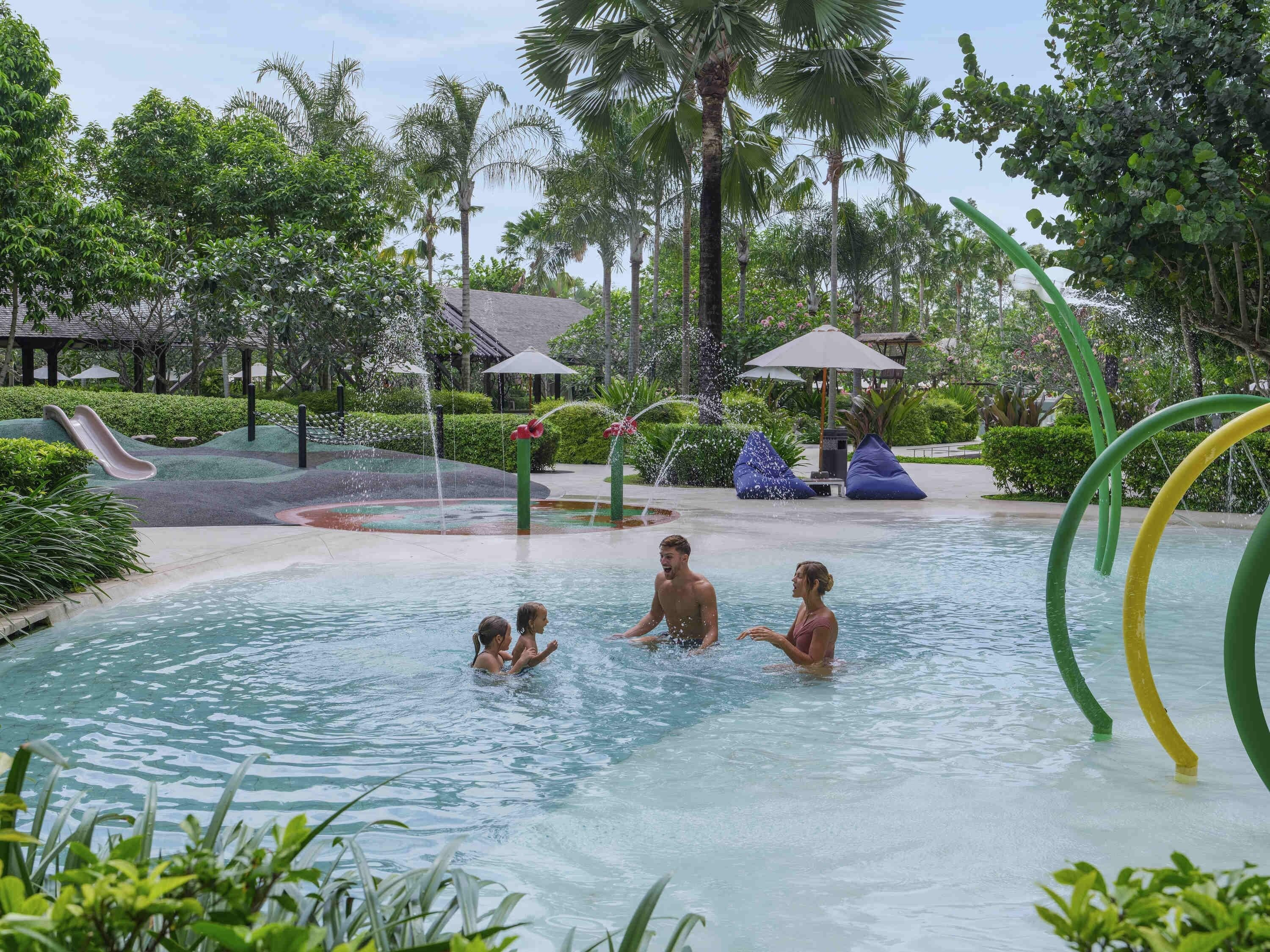 A swimming pool area with water slides, palm trees, and umbrellas.