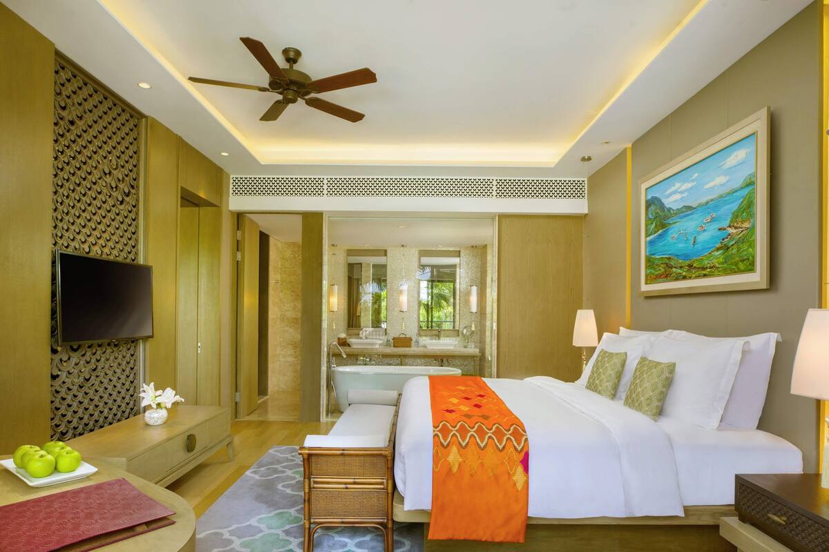 A hotel room with a bed, bedside table, TV, and a painting on the wall.