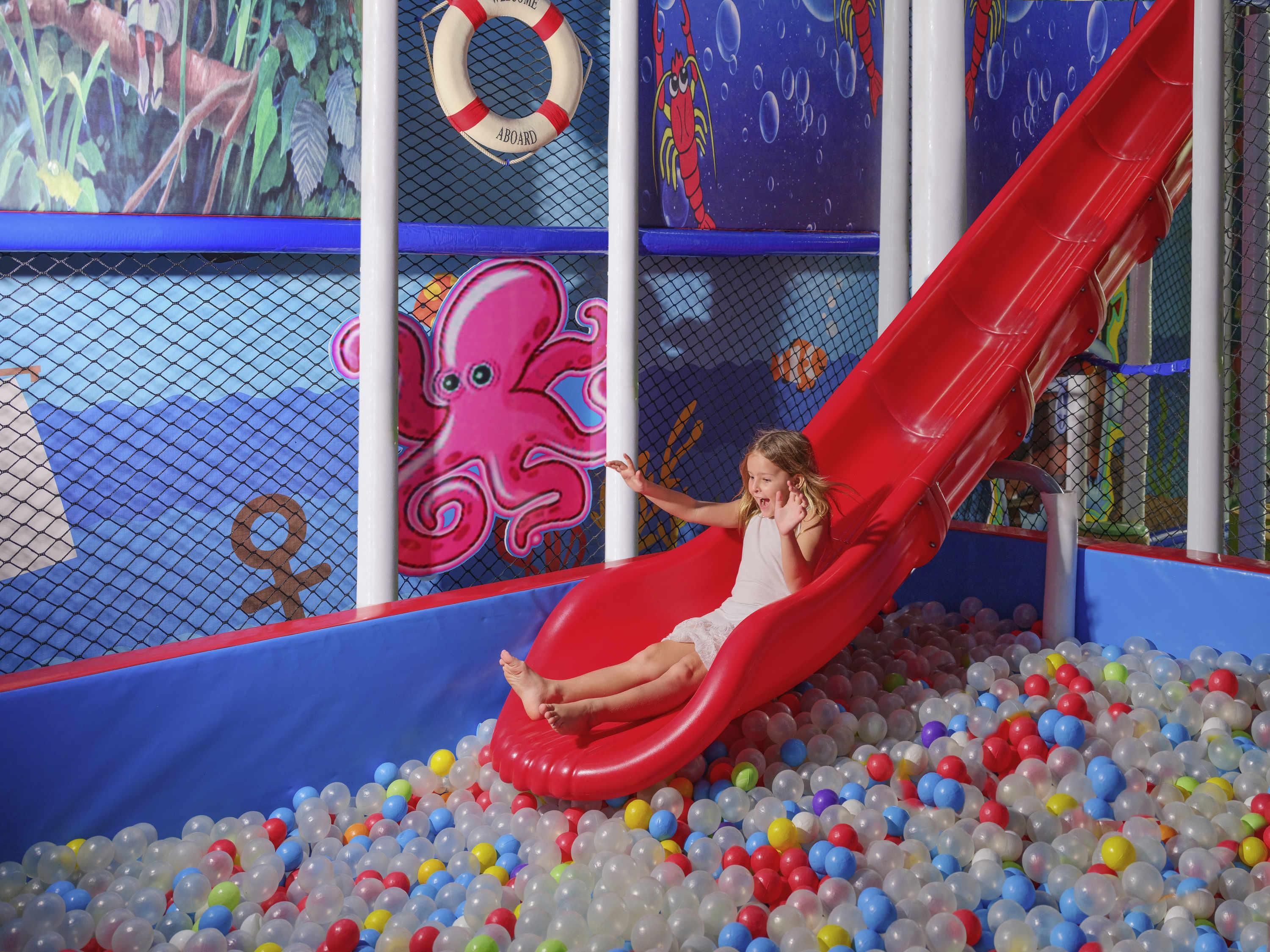 Un bambino scivola su uno scivolo rosso in una piscina piena di palline di plastica colorate.