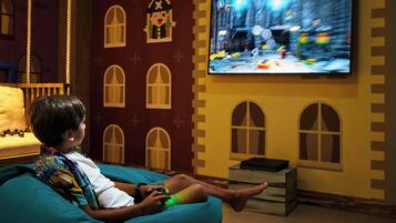 A child playing a video game on a couch in a room with a large TV mounted on the wall.