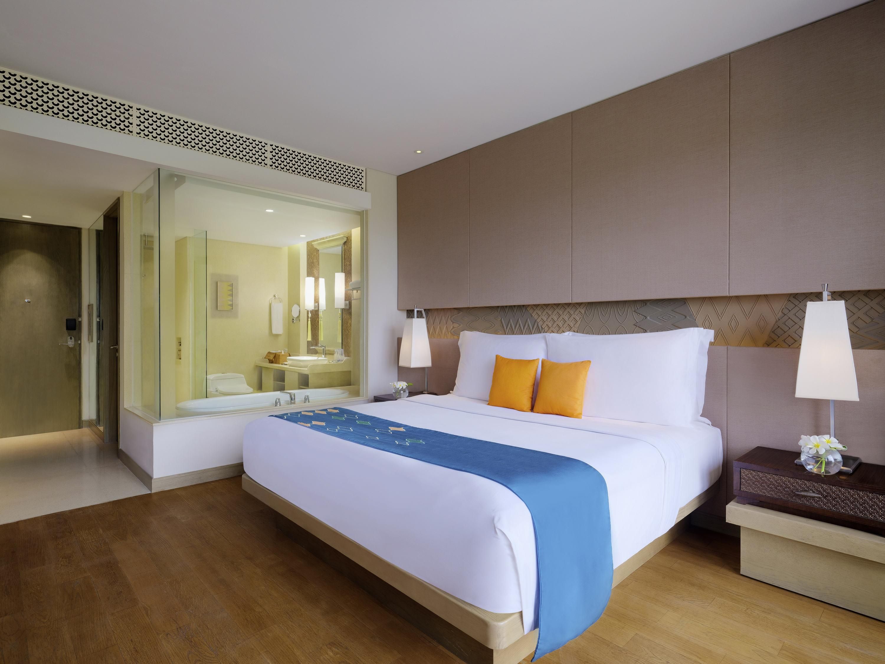 Ein Hotelzimmer mit Bett, Nachttisch, Lampe und einem Badezimmer mit Spiegel und Waschbecken.