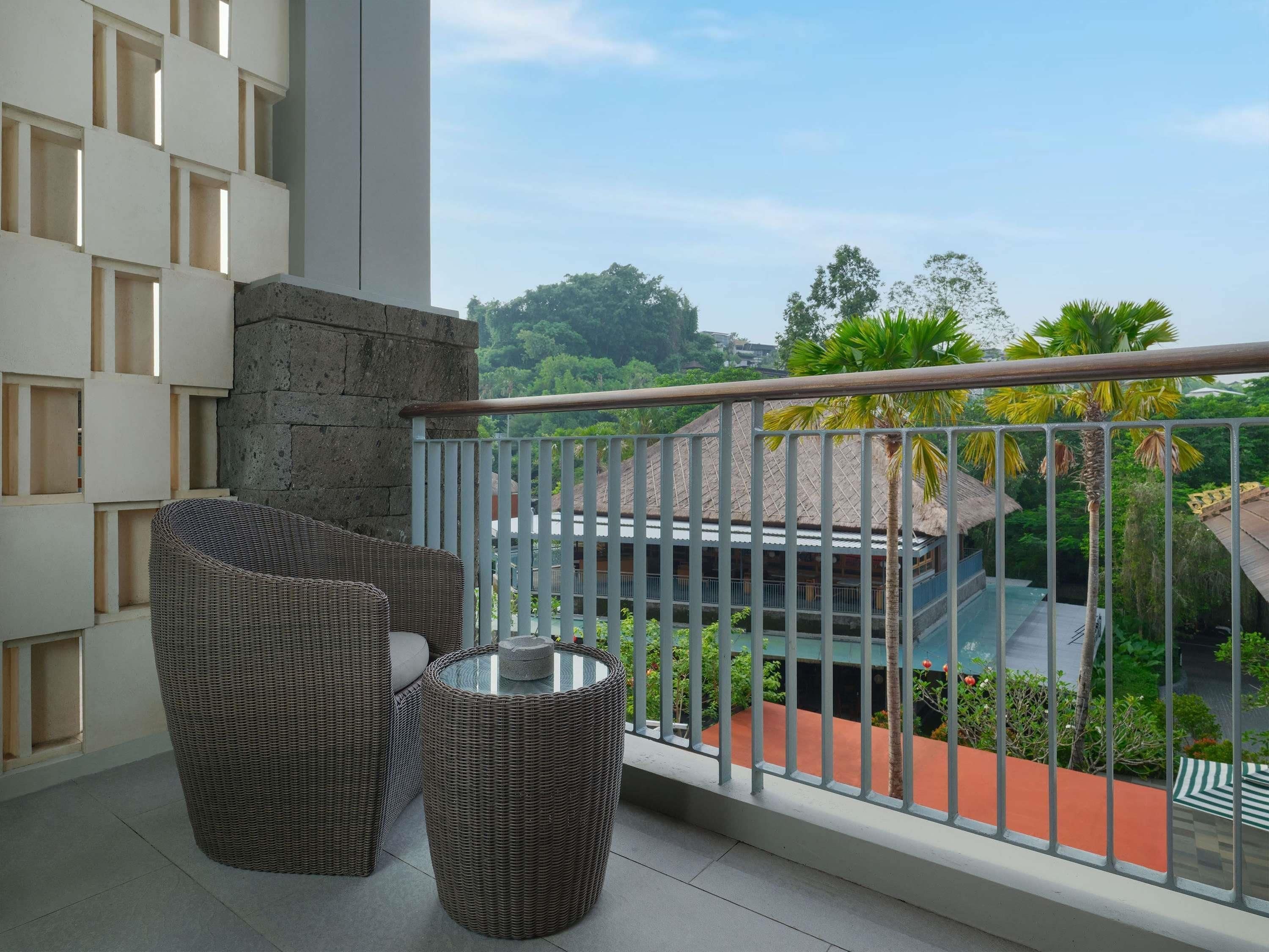 Un balcon agrémenté de meubles en osier, d’une table en verre et offrant une vue sur un bâtiment doté d’un toit de chaume.