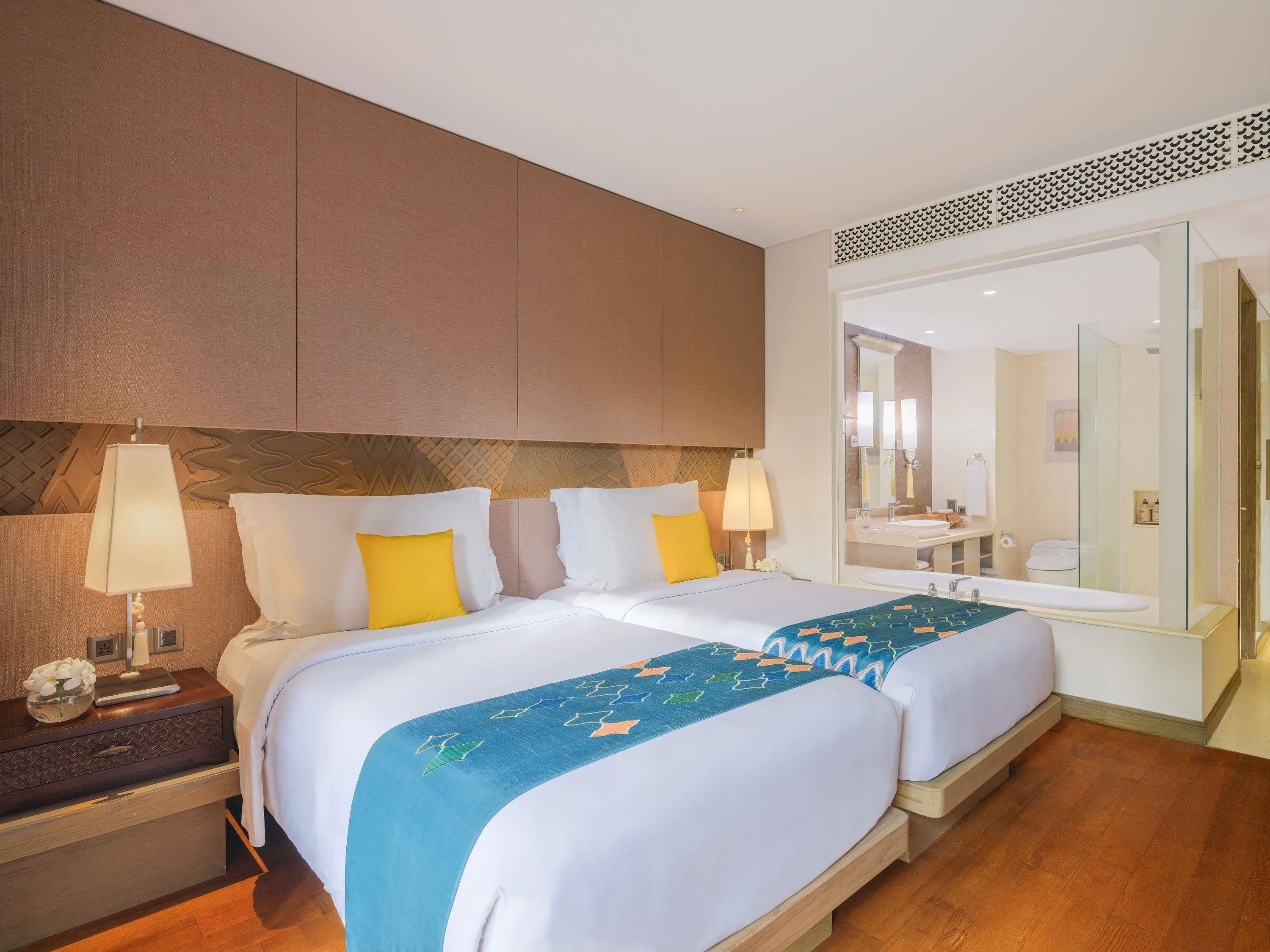 A hotel room with two beds, a large mirror, a bathroom with a sink and toilet, and a wooden floor.