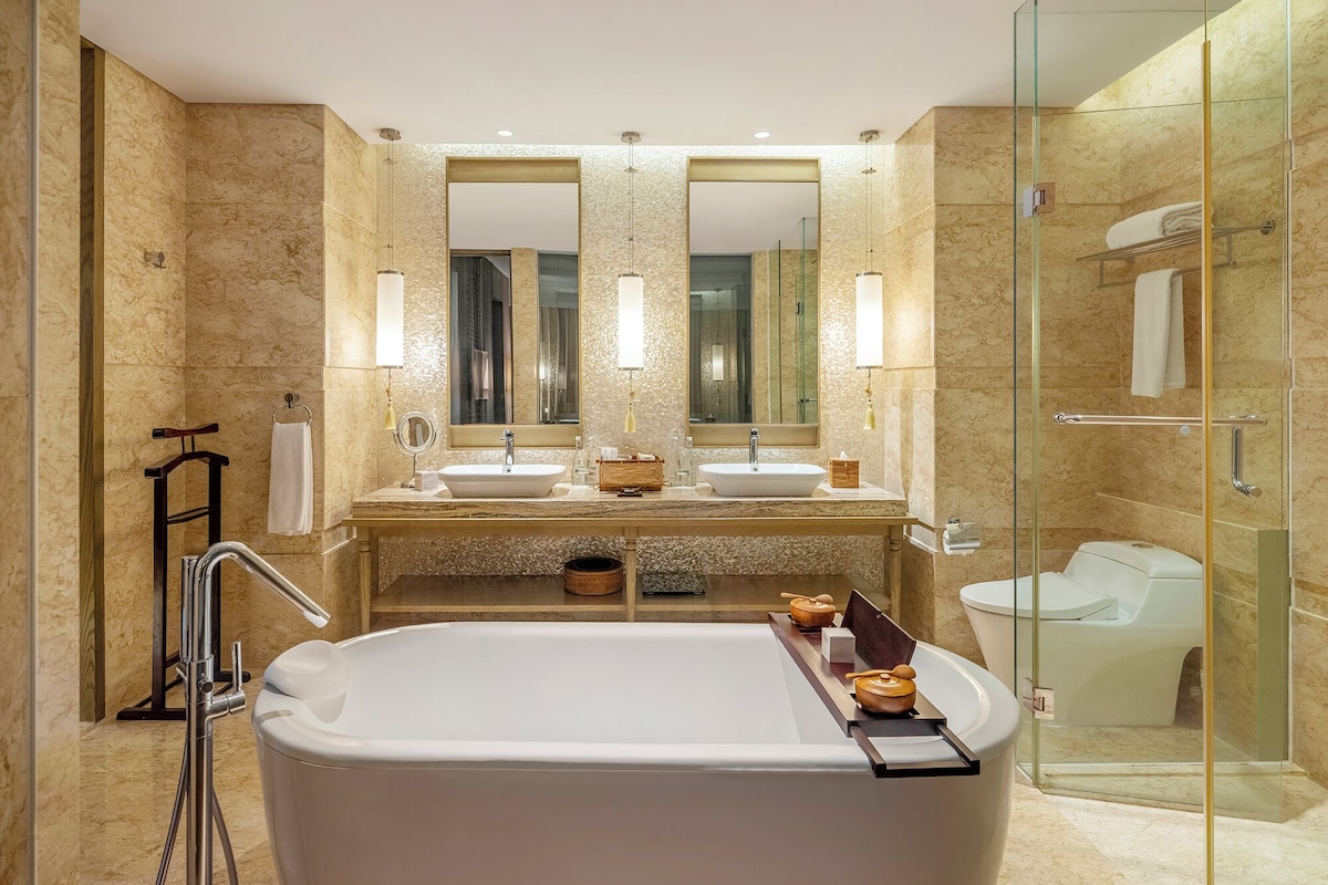 A modern bathroom with a large bathtub, two sinks, a glass-enclosed shower, and a large mirror.