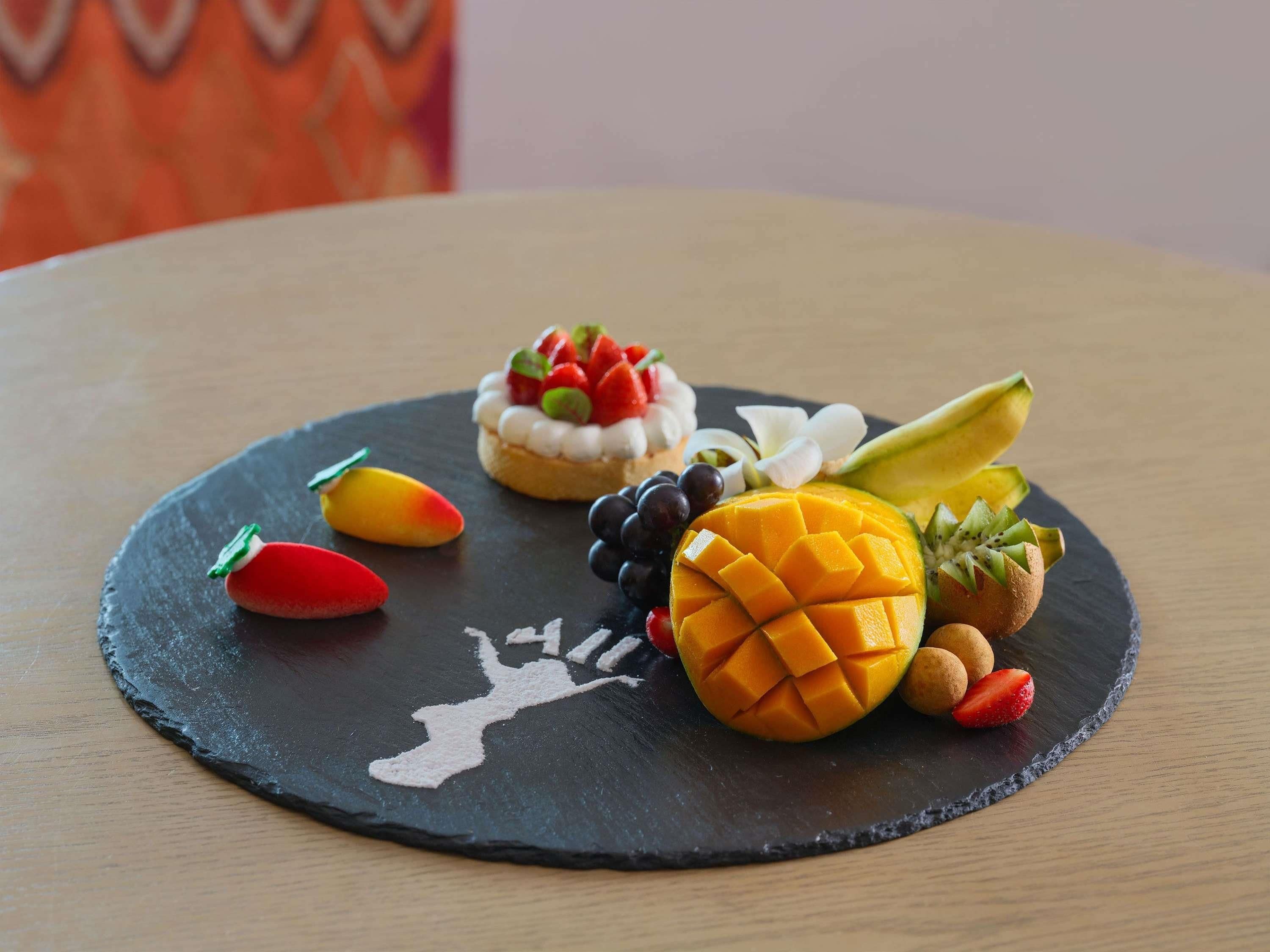 A round black slate table with a dessert and various fruits.