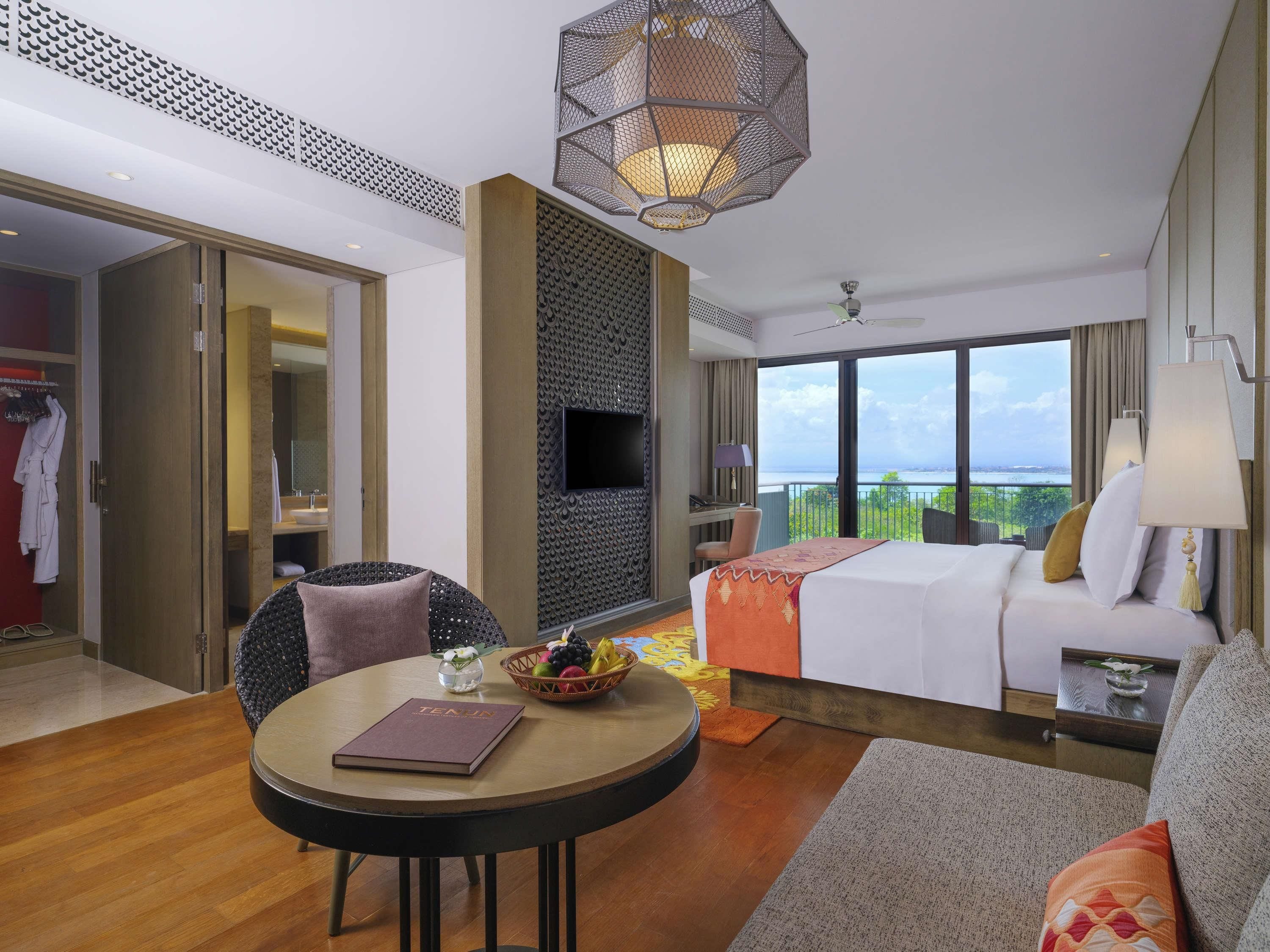 A hotel room with a bed, a desk, a chair, a round table, and a large window with a view.