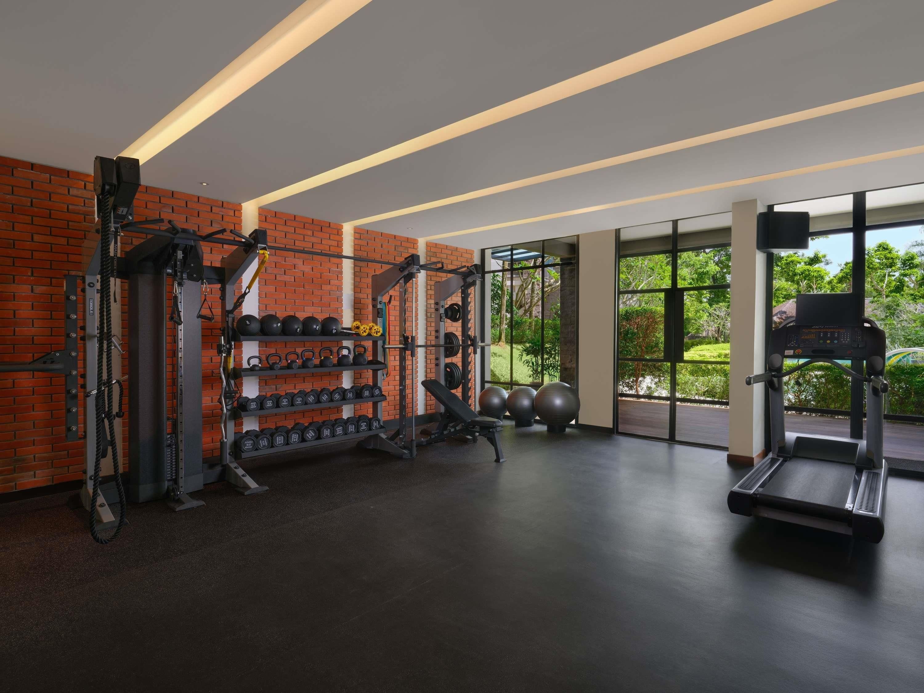 Un gimnasio con equipo de ejercicio, pared de ladrillo y amplios ventanales.