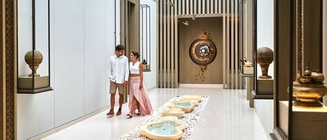 A modern hotel lobby with a central water feature, a decorative wall, and a patterned floor.