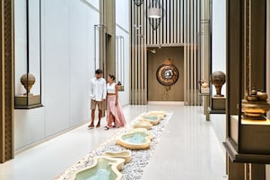 A modern hotel lobby with a central water feature, a decorative wall, and a patterned floor.