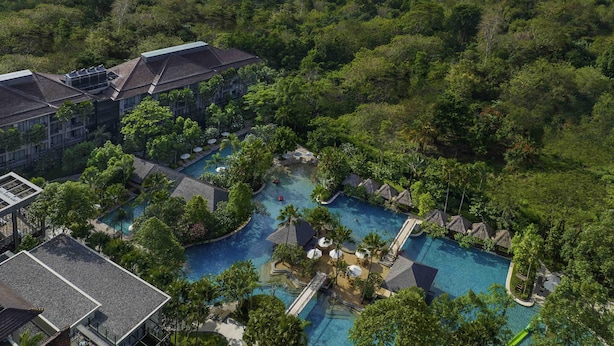 A resort with multiple swimming pools surrounded by lush greenery and a view of the ocean.