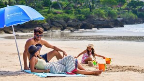 Een strandscène met een blauwe parasol met de tekst 'Mövenpick Resort & Spa Jimbaran Bali'.