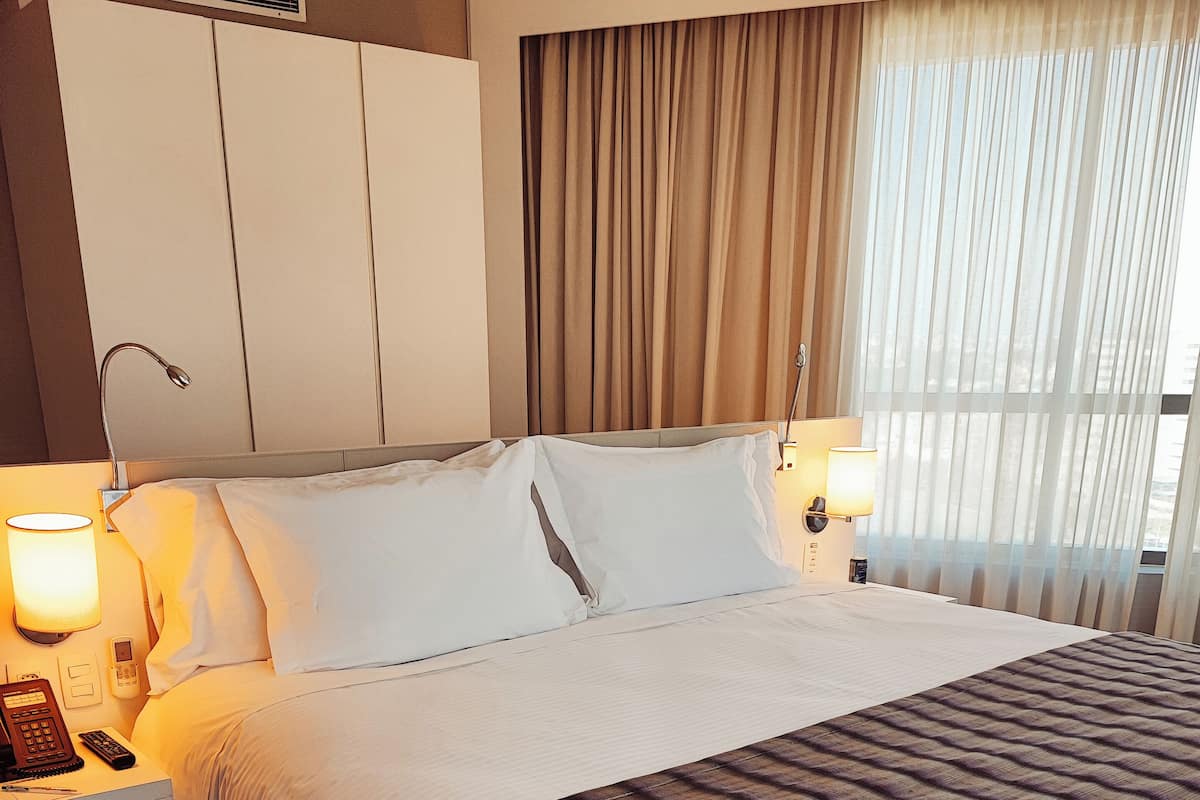 Une chambre d’hôtel avec un grand lit, deux tables de chevet, un téléphone et une lampe.