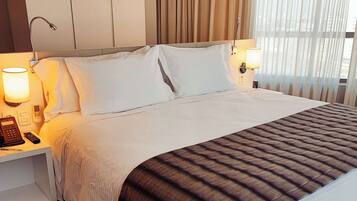 A neatly made bed with white linens and a striped blanket, bedside lamps, a telephone, and a nightstand.