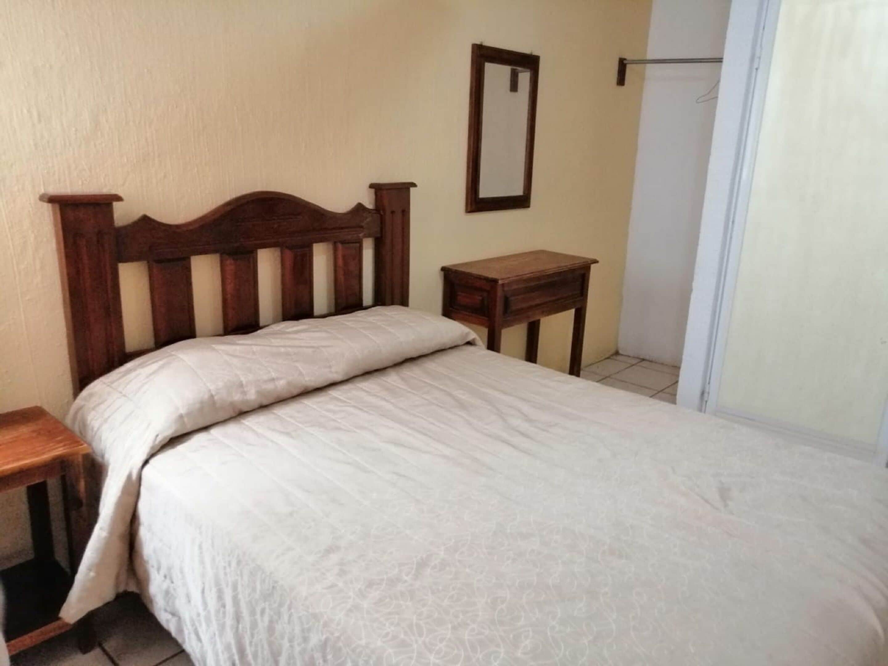 A bedroom with a wooden bed frame, a small bedside table, and a mirror on the wall.