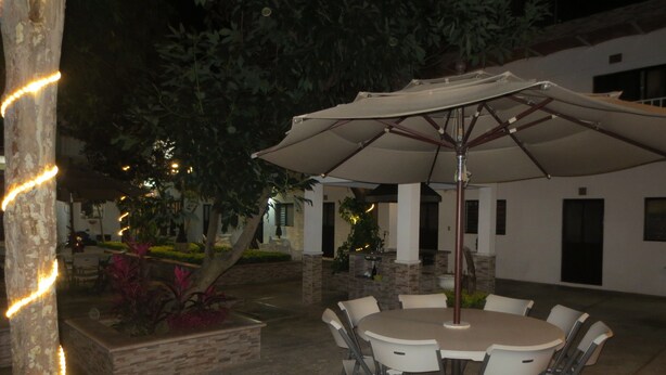 An outdoor patio with a round table and chairs, surrounded by a white building with columns and a stone pathway. - Hotel Arboledas (Talpa de Allende)