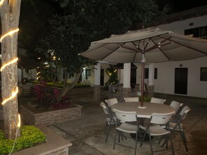 An outdoor patio with a round table and chairs, surrounded by a white building with columns and a stone pathway. - Hotel Arboledas (Talpa de Allende)