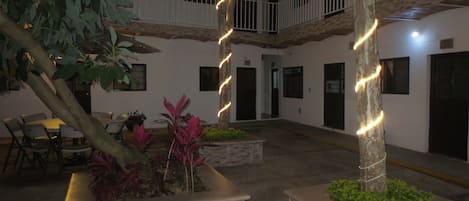 Un patio con un árbol, macetas y un edificio con varias puertas y ventanas.