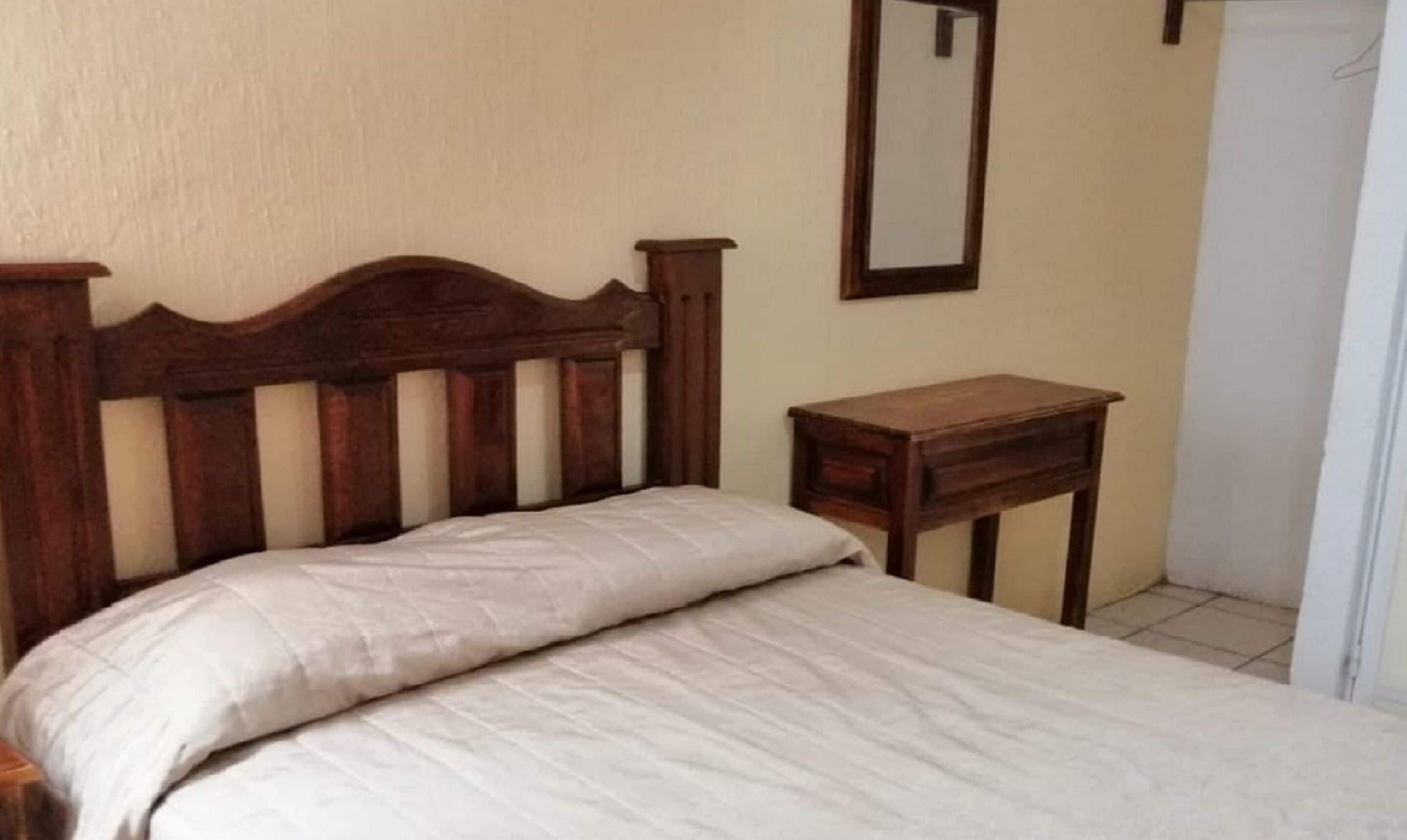 Una camera da letto con una testiera in legno, un letto singolo con materasso bianco e un comodino in legno.