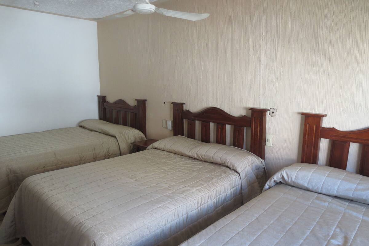 Een kamer met drie eenpersoonsbedden, elk met houten hoofdeinden en beige beddengoed.