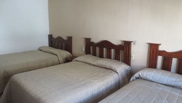 Een kamer met drie eenpersoonsbedden, elk met houten hoofdeinden en beige beddengoed.