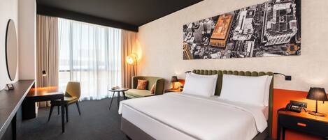 A hotel room with a large bed, a desk, a chair, a sofa, and a cityscape painting on the wall.