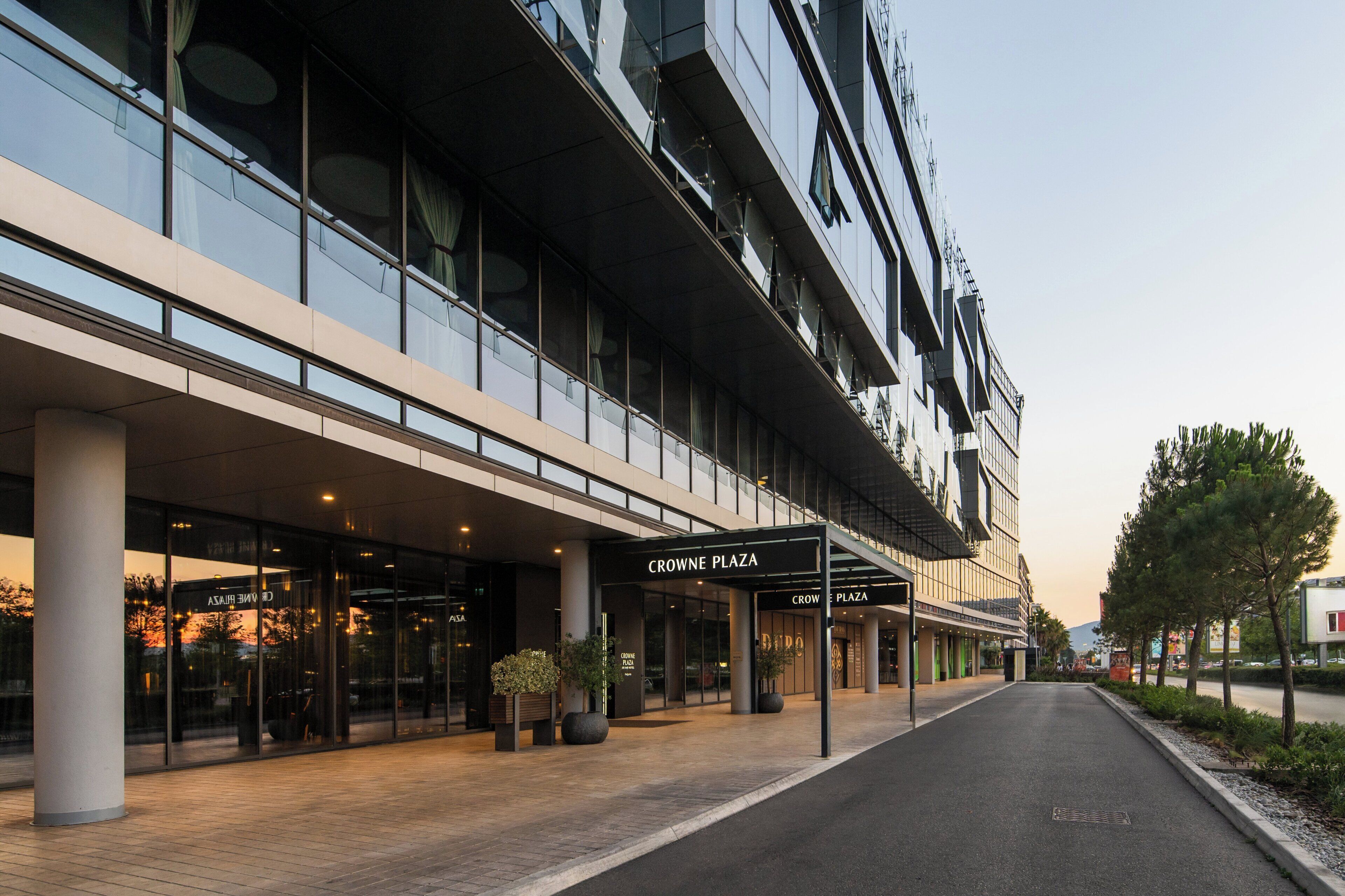 Un bâtiment moderne doté d’une façade en verre, d’une entrée couverte et d’une enseigne indiquant « CROWNE PLAZA ».