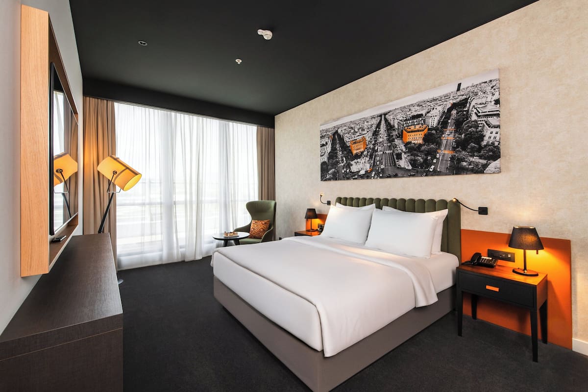 Une chambre d’hôtel moderne, dotée d’un grand lit, d’un bureau, d’une chaise et d’une grande fenêtre avec des rideaux.