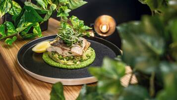 Prato de comida com molho verde, peixe, folhos verdes e um gomo de limão.