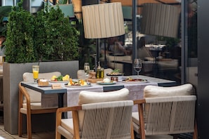An outdoor dining area with a table set for two, featuring a variety of dishes, a wine glass, and a bottle of olive oil. - Crowne Plaza Podgorica by IHG (Podgorica)