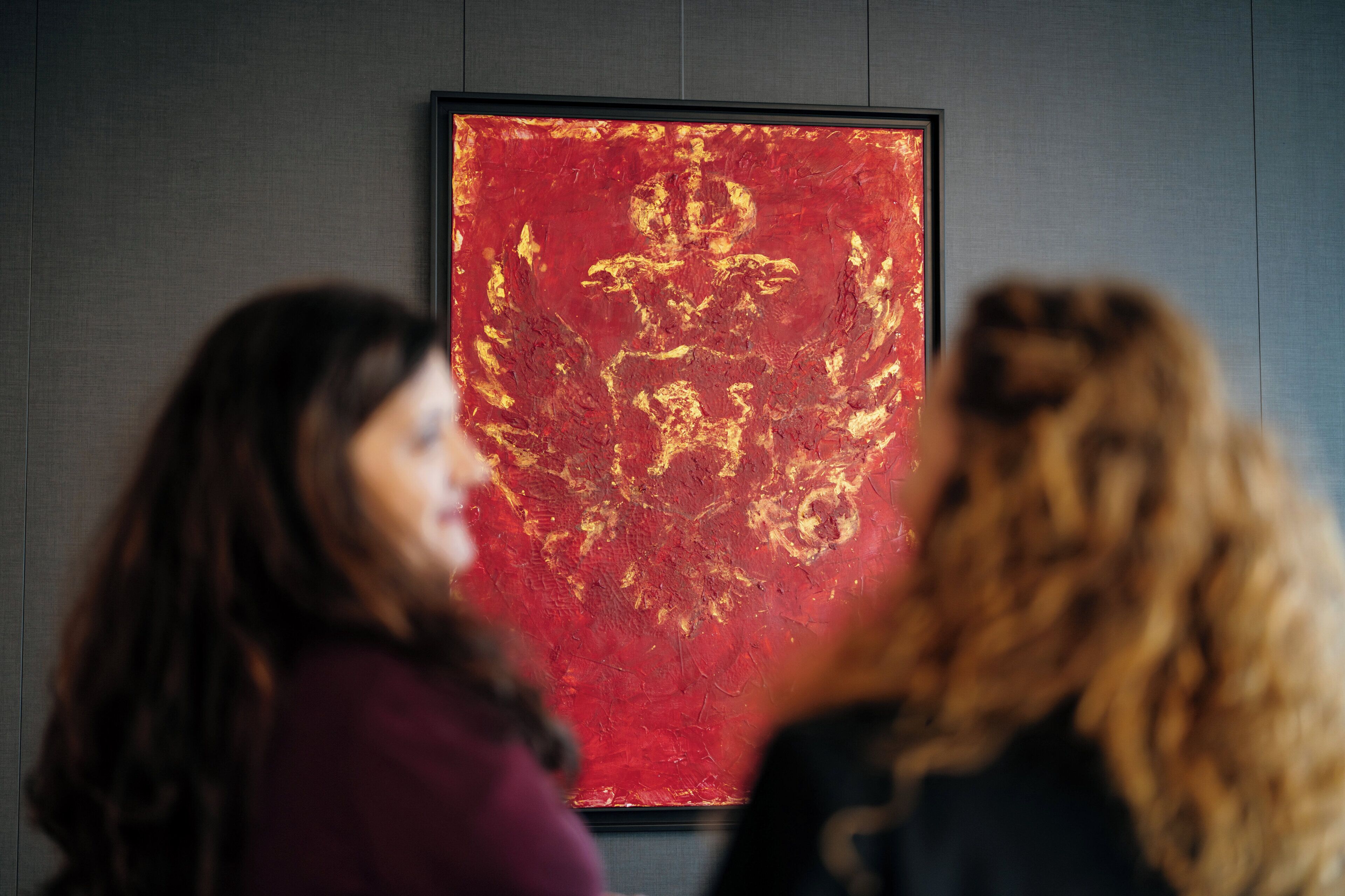 Two people viewing a framed artwork on a wall.