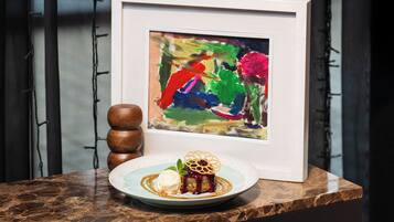A dessert plate with a cake and ice cream on a marble countertop, a framed painting, and a wooden object.