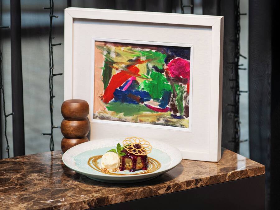 A dessert plate with a cake and ice cream on a marble countertop, a framed painting, and a wooden object.